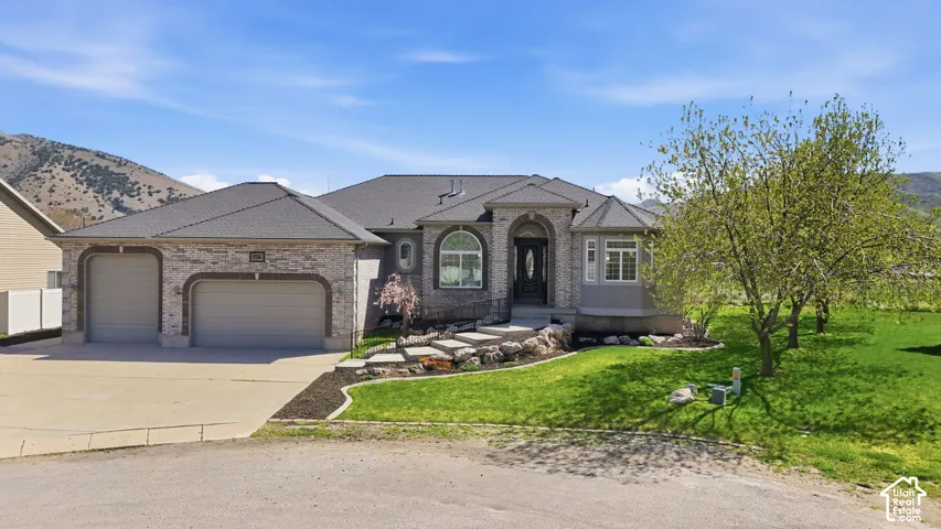 French country style house featuring a front lawn, a garage, driveway, brick siding, and a mountain view