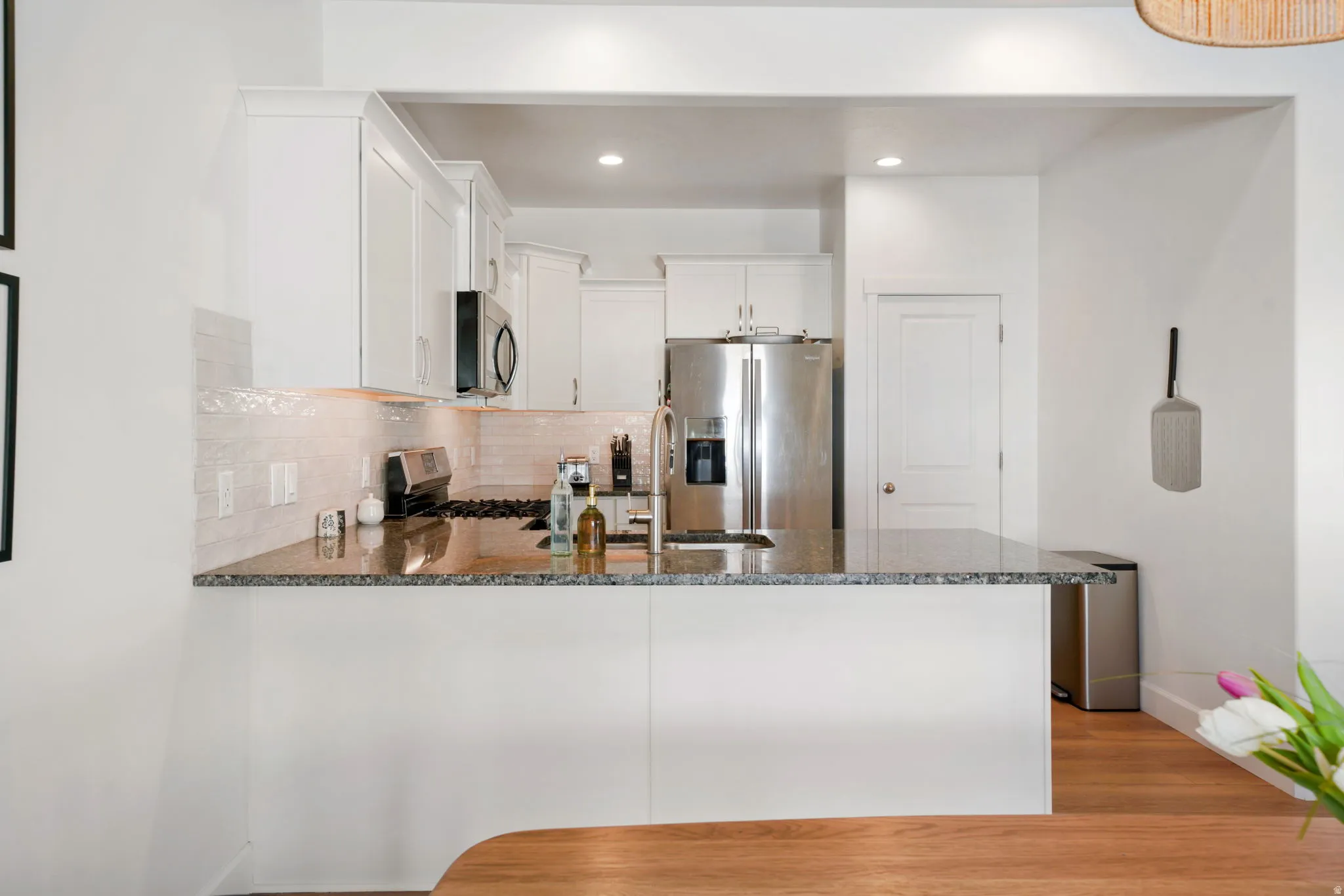 Kitchen with dark stone counters, white cabinets, stainless steel appliances, a peninsula, and decorative backsplash