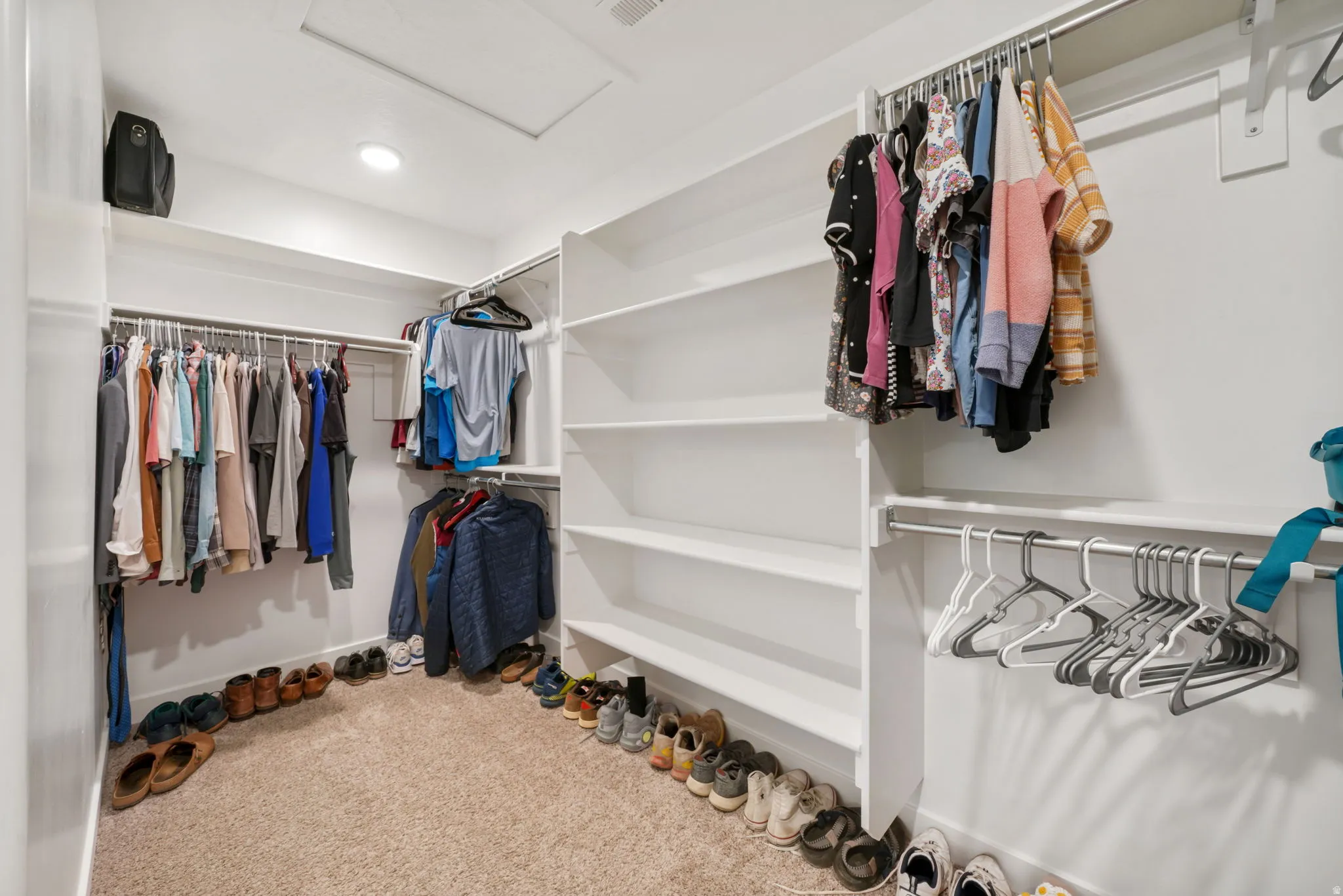 Walk in closet with attic access and light colored carpet