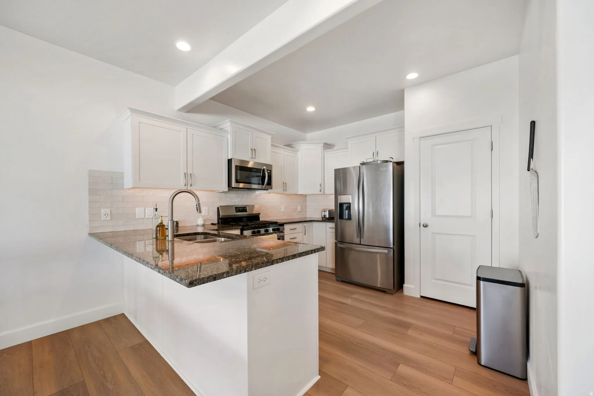 Kitchen featuring a peninsula, stainless steel appliances, beam ceiling, dark stone counters, and white cabinets