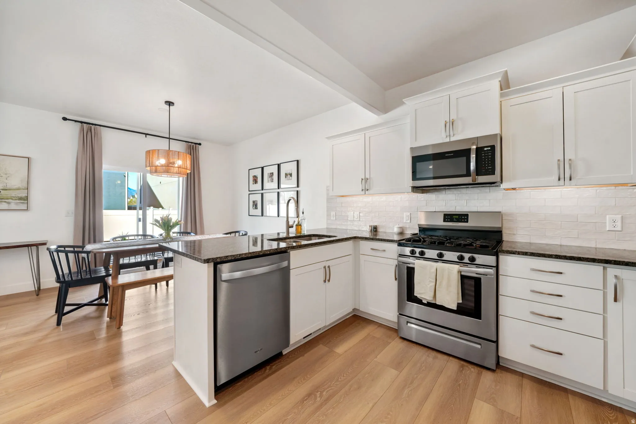 Kitchen featuring stainless steel appliances, white cabinetry, a peninsula, dark stone countertops, and beam ceiling