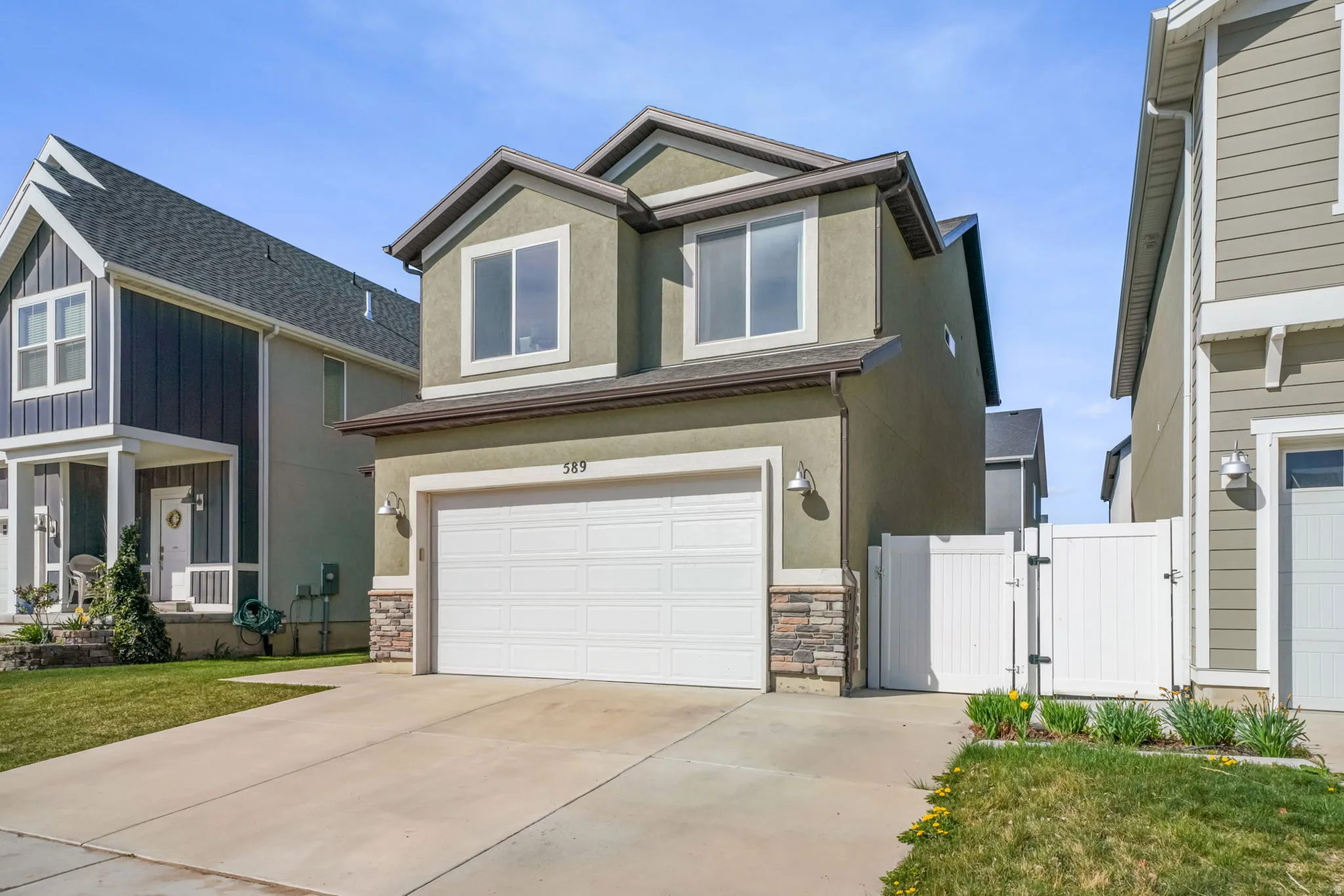 View of front of home with a gate, stucco siding, stone siding, a garage, and driveway