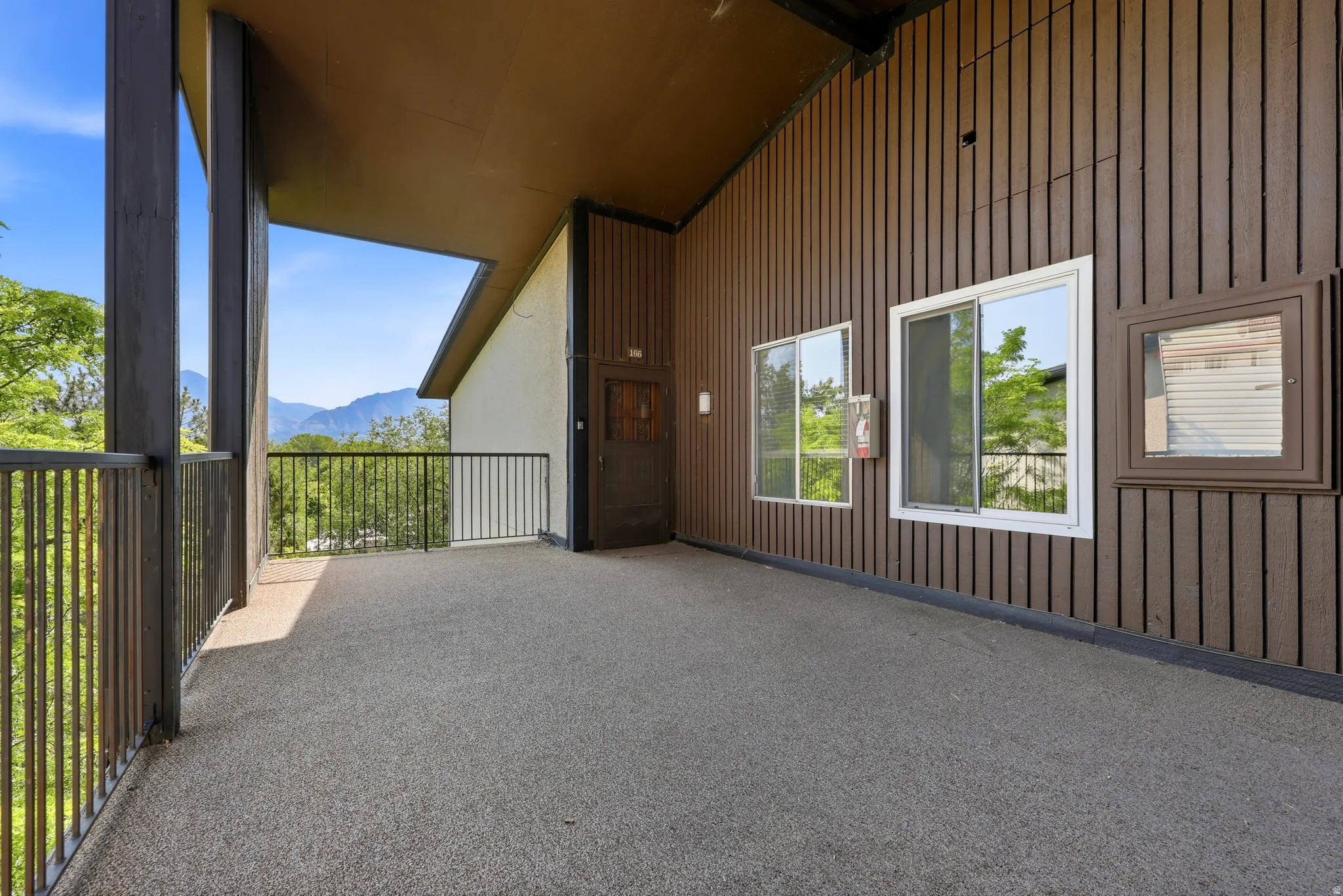 Private outdoor balcony with a textured concrete surface, metal railings, and mountain scenery