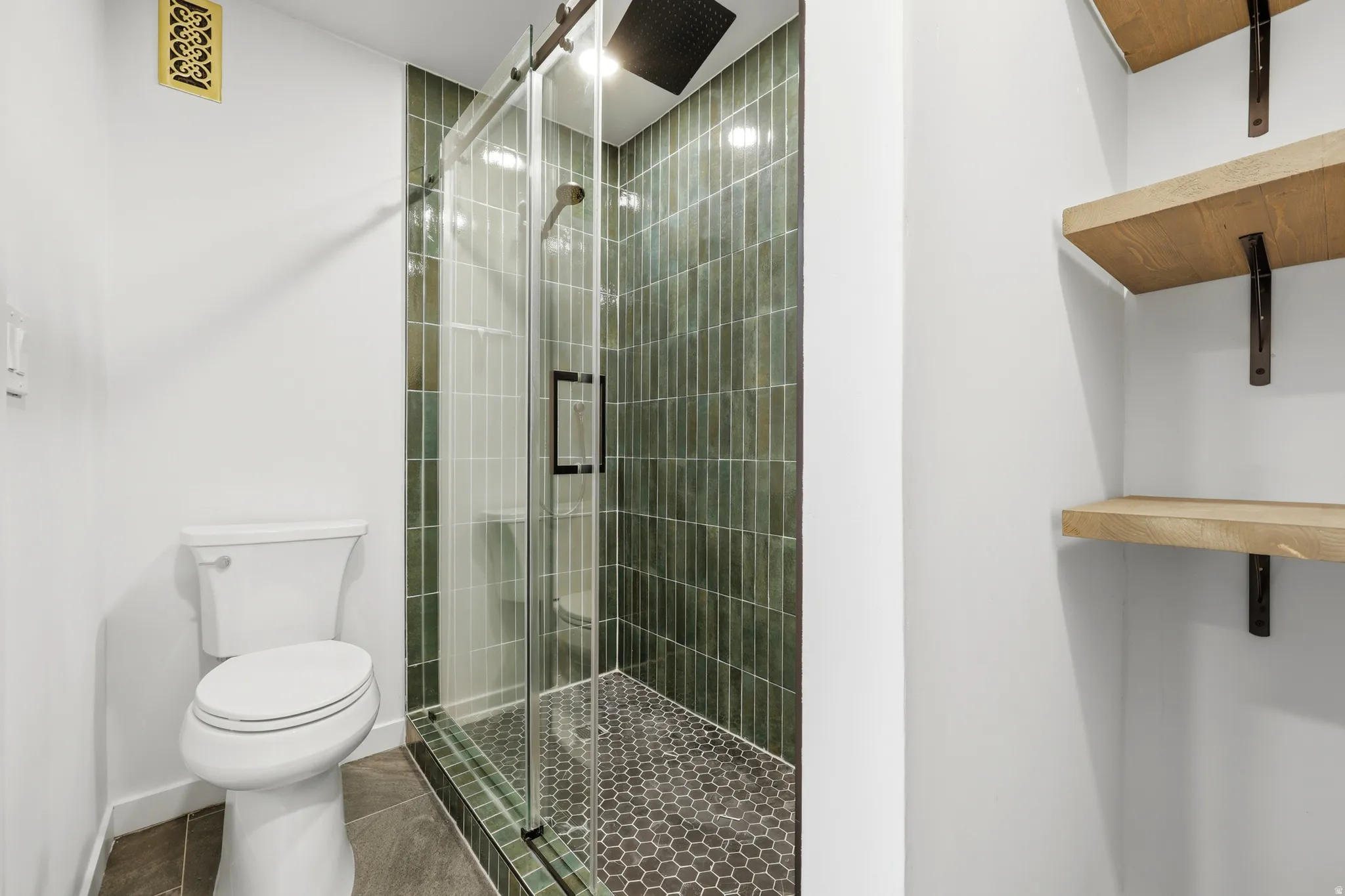 Bathroom featuring a frameless glass shower enclosure with dark green vertical tile, a rain shower head, and hexagon mosaic floor tile