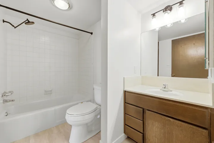 Bathroom featuring a white subway-tiled shower/tub combination, a vanity with a light-toned countertop, a rectangular mirror, and a three-light fixture