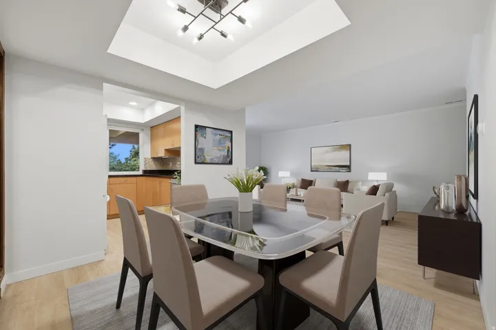 Open-concept dining area featuring a tray ceiling with a linear chandelier, wood-finish flooring, and white baseboards. Virtually Staged.