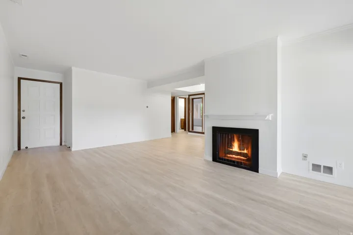 Spacious living area featuring light wood-finish flooring and a built-in fireplace with a black surround and white mantel