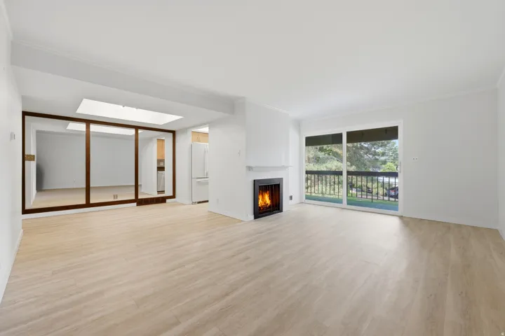 Spacious living area featuring light wood-finish flooring, a contemporary fireplace, and white walls