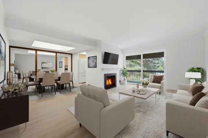 Open-concept living area featuring a fireplace, wood-finish flooring, a full-lite glass door to the exterior, a large mirror wall, and an overhead skylight. Virtual Staging.