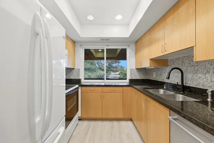 Kitchen featuring abundant light wood cabinetry, dark countertops, a mosaic tile backsplash, and light wood-finish flooring