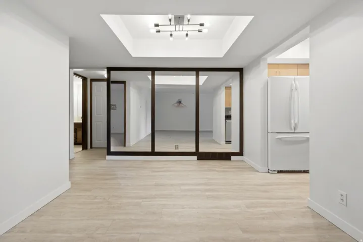 Recessed ceiling with modern chandelier, light wood-finish flooring, and white walls