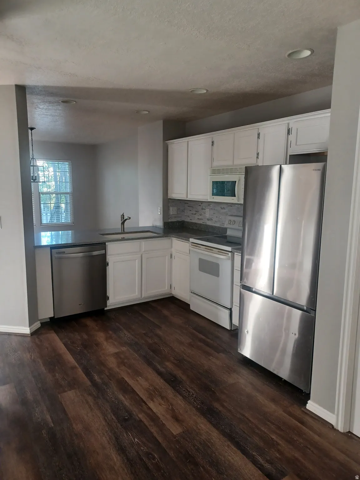 Kitchen with stainless steel appliances, white cabinets, dark countertops, dark wood-type flooring, and recessed lighting