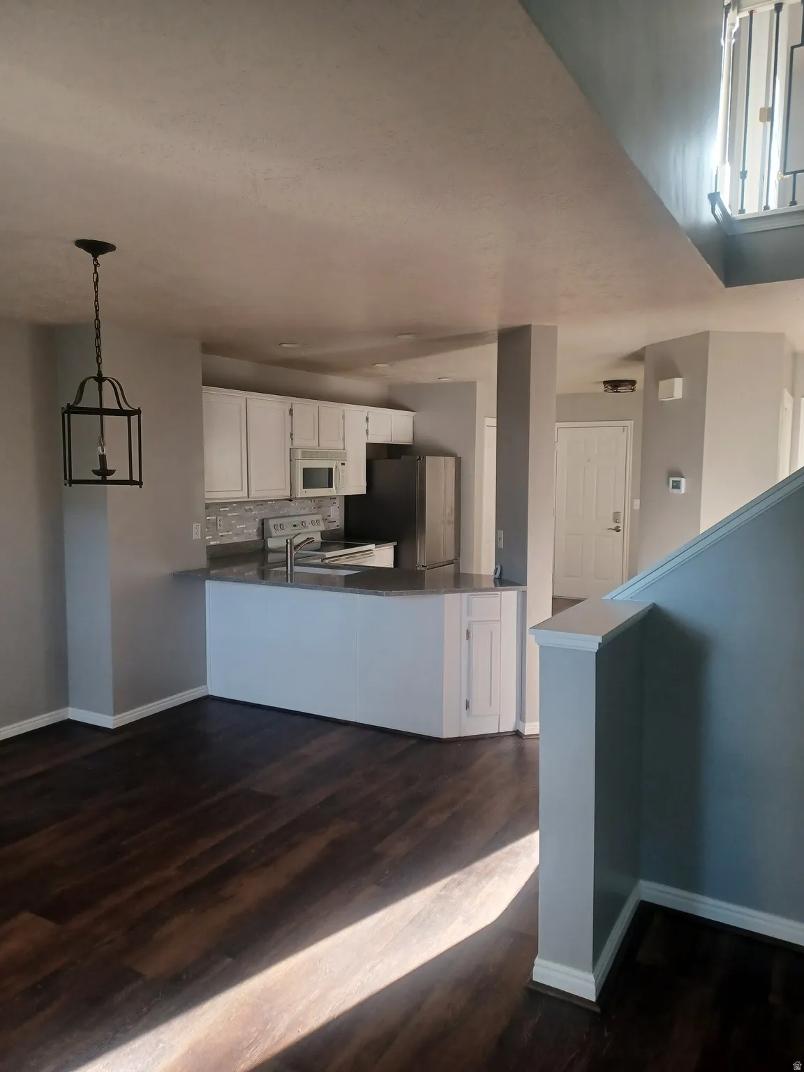 Kitchen with white cabinetry, a peninsula, dark countertops, white appliances, and dark wood finished floors