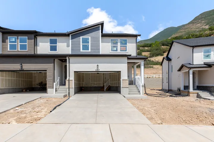 Contemporary townhome exterior featuring an attached two-car garage, concrete driveway, and a white railing leading to the front entry