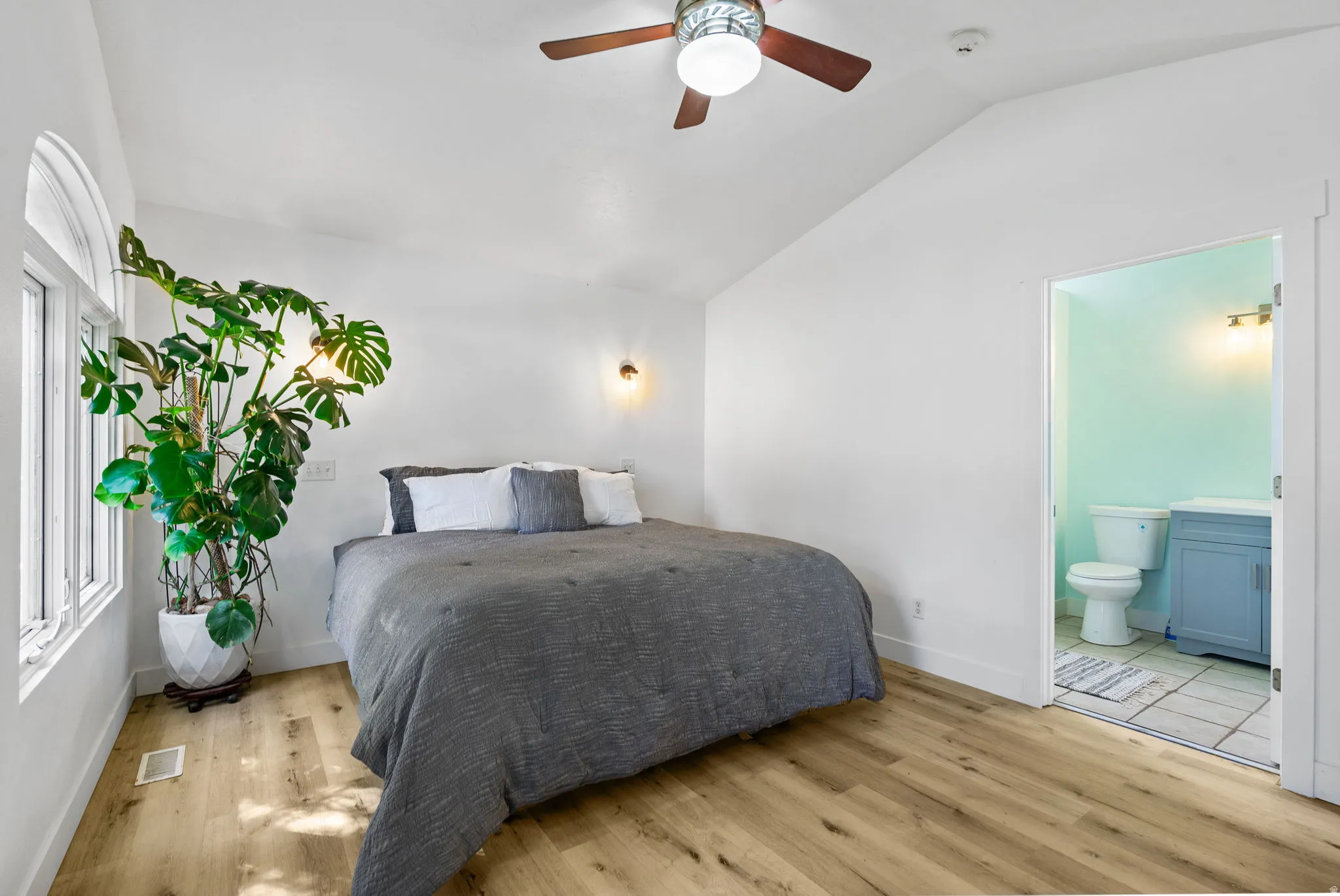 Primary Bedroom featuring light wood-style floors, lofted ceiling, ceiling fan, and connected bathroom