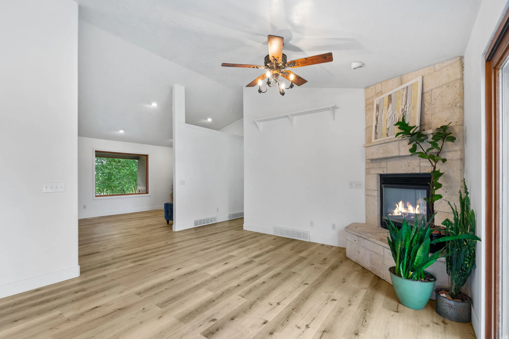 Unfurnished living room with a stone fireplace, a ceiling fan, lofted ceiling, and light wood finished floors