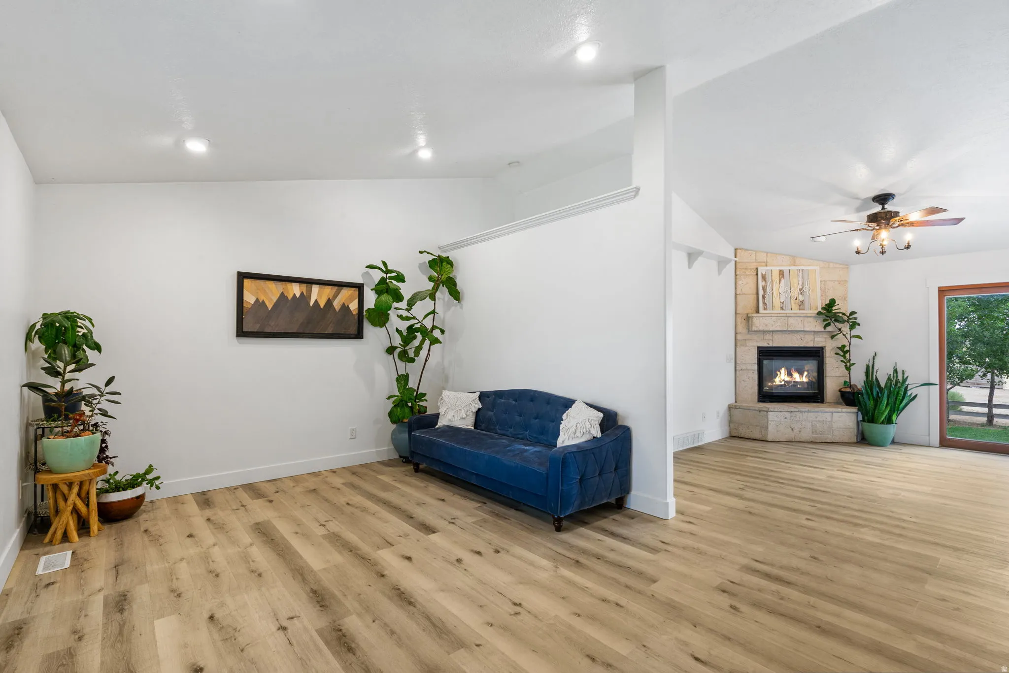 Living area featuring lofted ceiling, light wood-style flooring, a tile fireplace, and ceiling fan