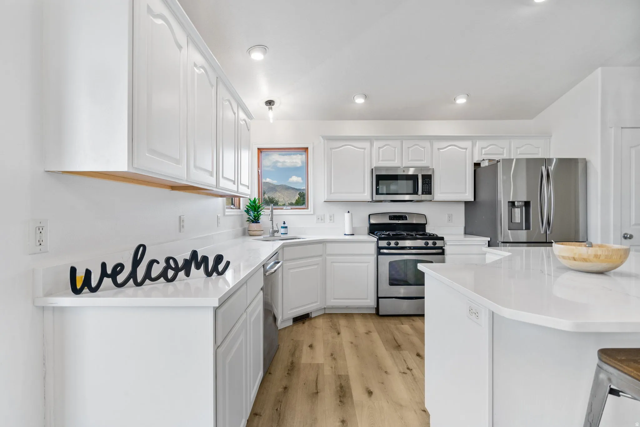 Kitchen featuring white cabinets, stainless steel appliances, light wood-style floors, recessed lighting, and light stone counters