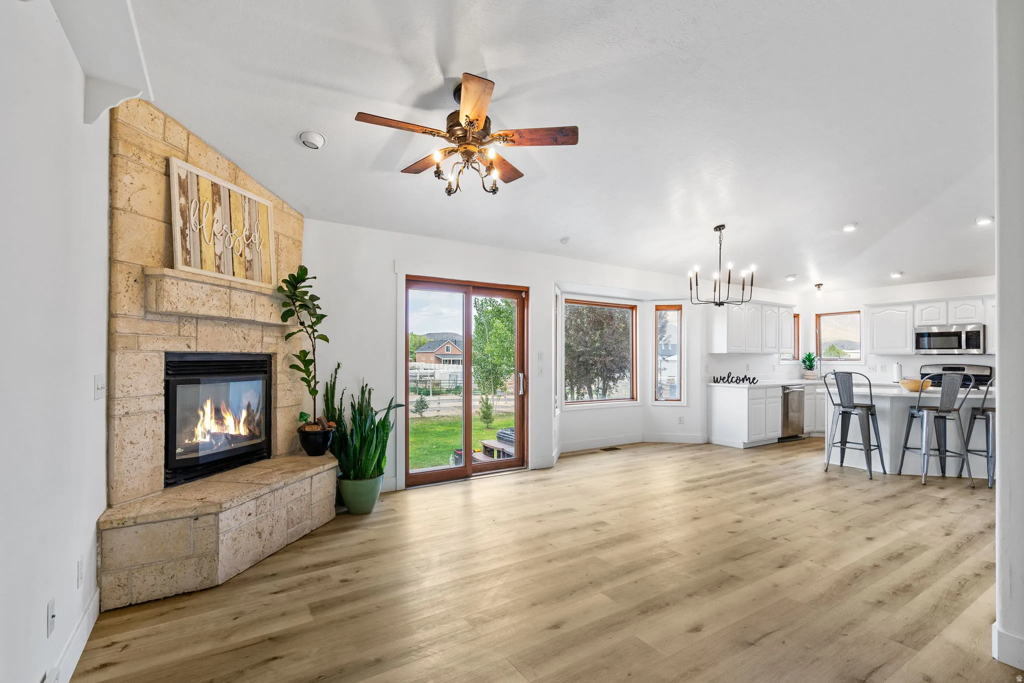 Unfurnished living room featuring vaulted ceiling, a fireplace, ceiling fan, suspended lighting, and light wood finished floors