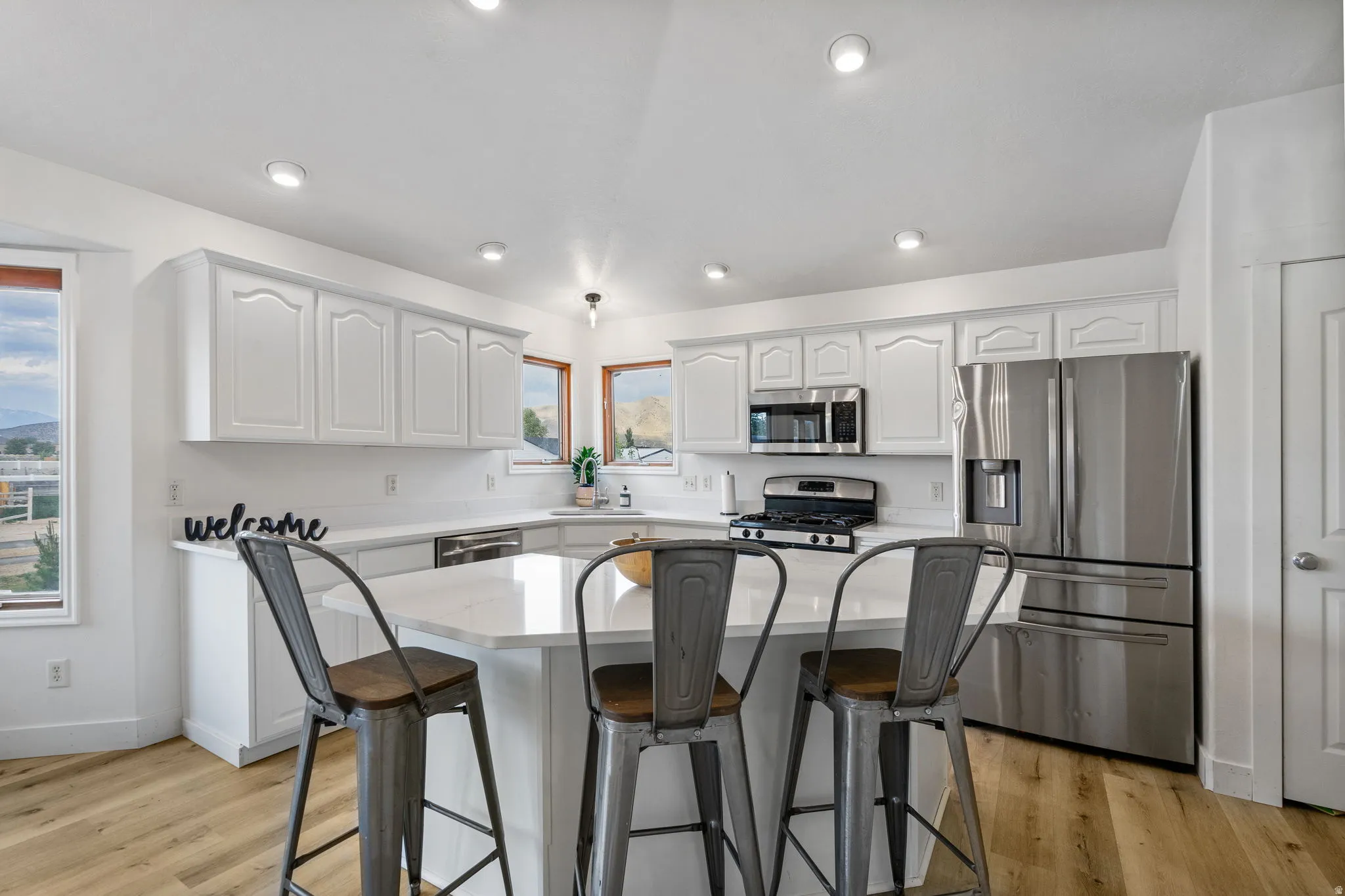 Kitchen with a breakfast bar area, stainless steel appliances, white cabinetry, a center island, and light wood-style flooring