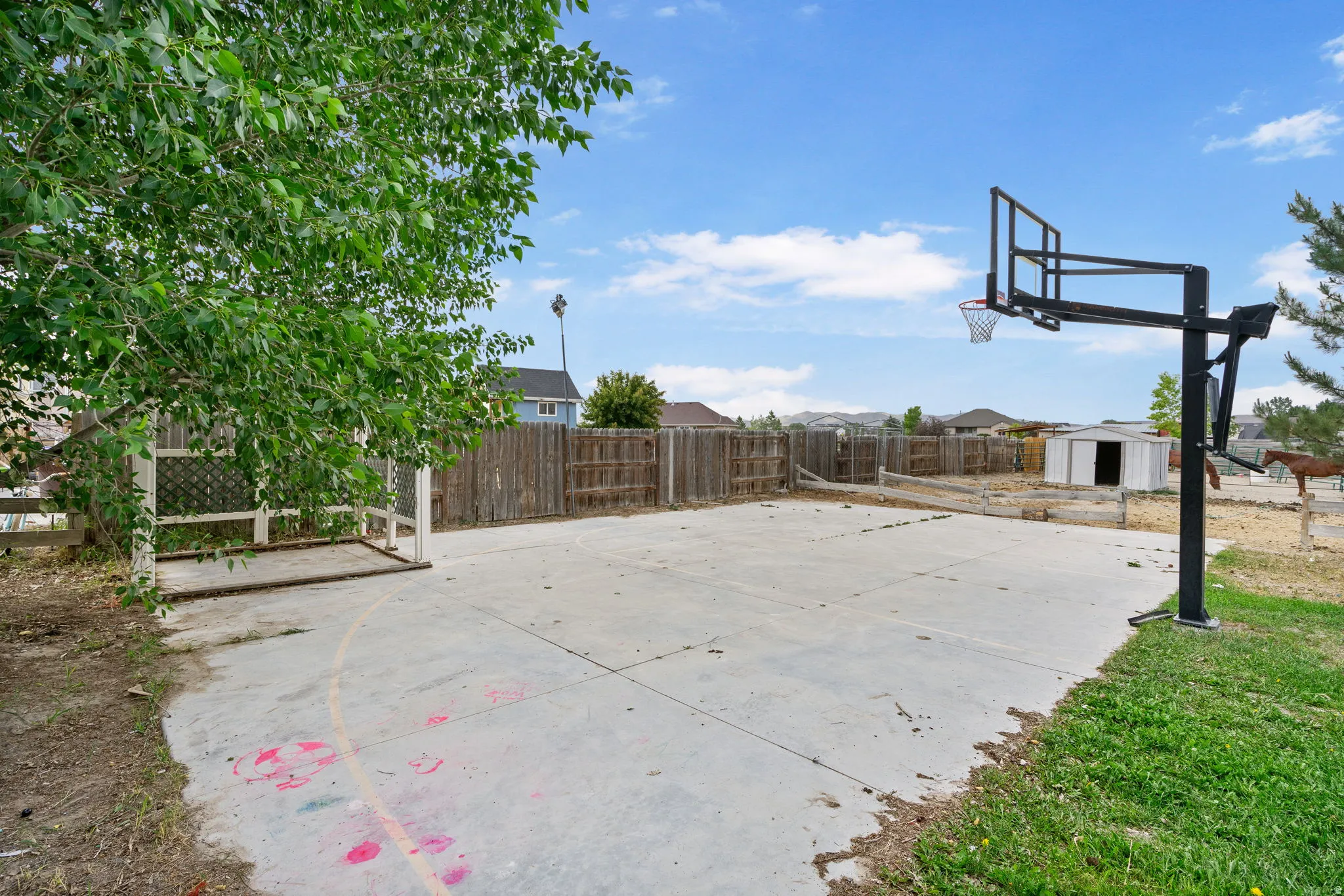 Fenced backyard with a shed, basketball court, and a residential view