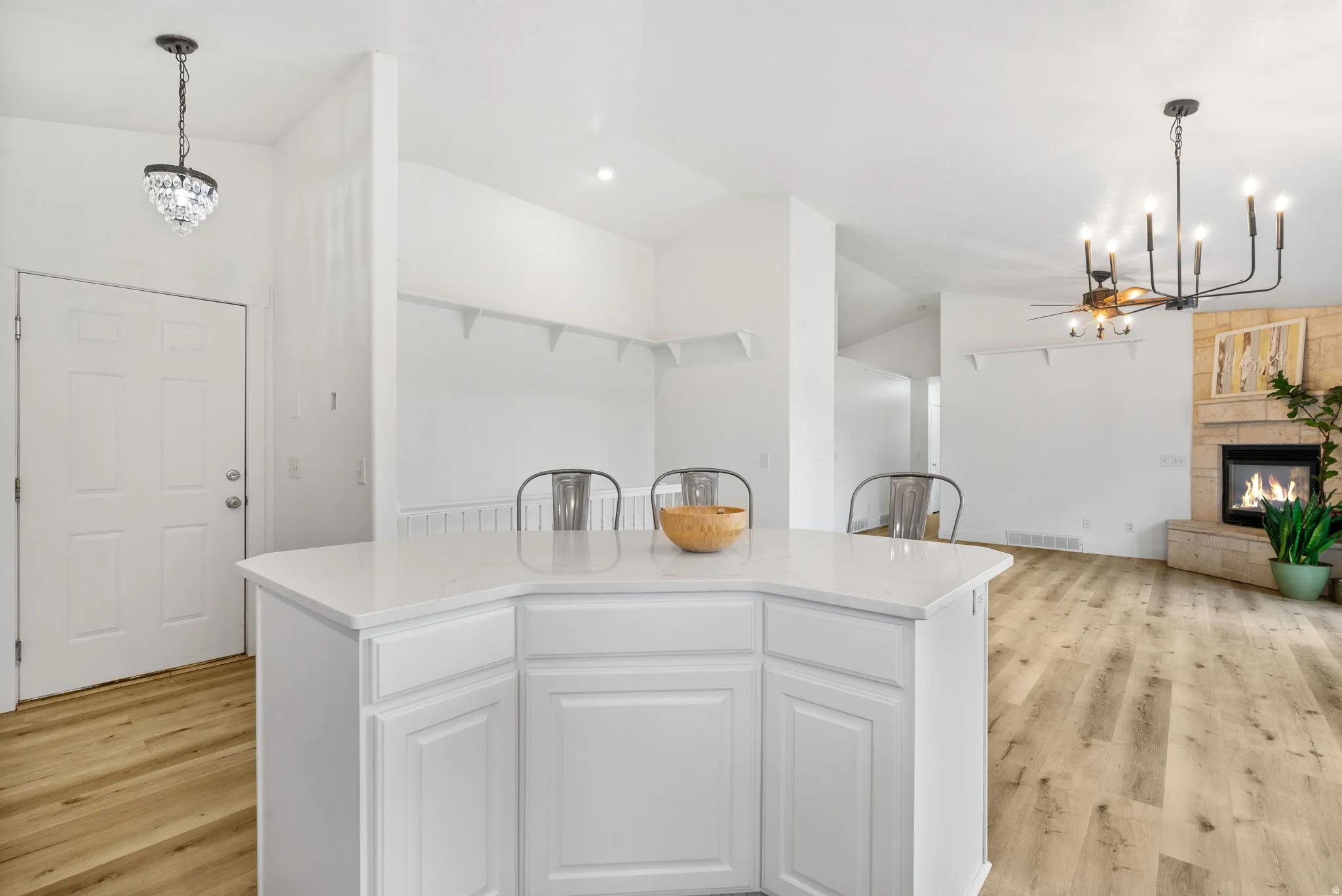 Kitchen featuring a chandelier, light wood finished floors, a glass covered fireplace, light stone counters, and lofted ceiling