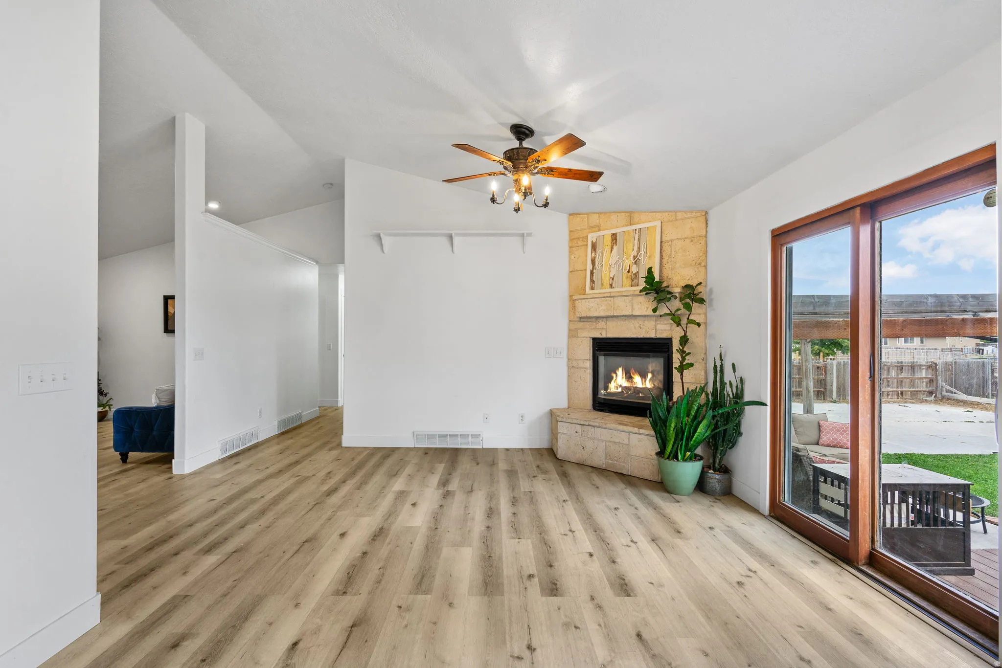 Unfurnished living room featuring ceiling fan, a stone fireplace, vaulted ceiling, and light wood-style flooring