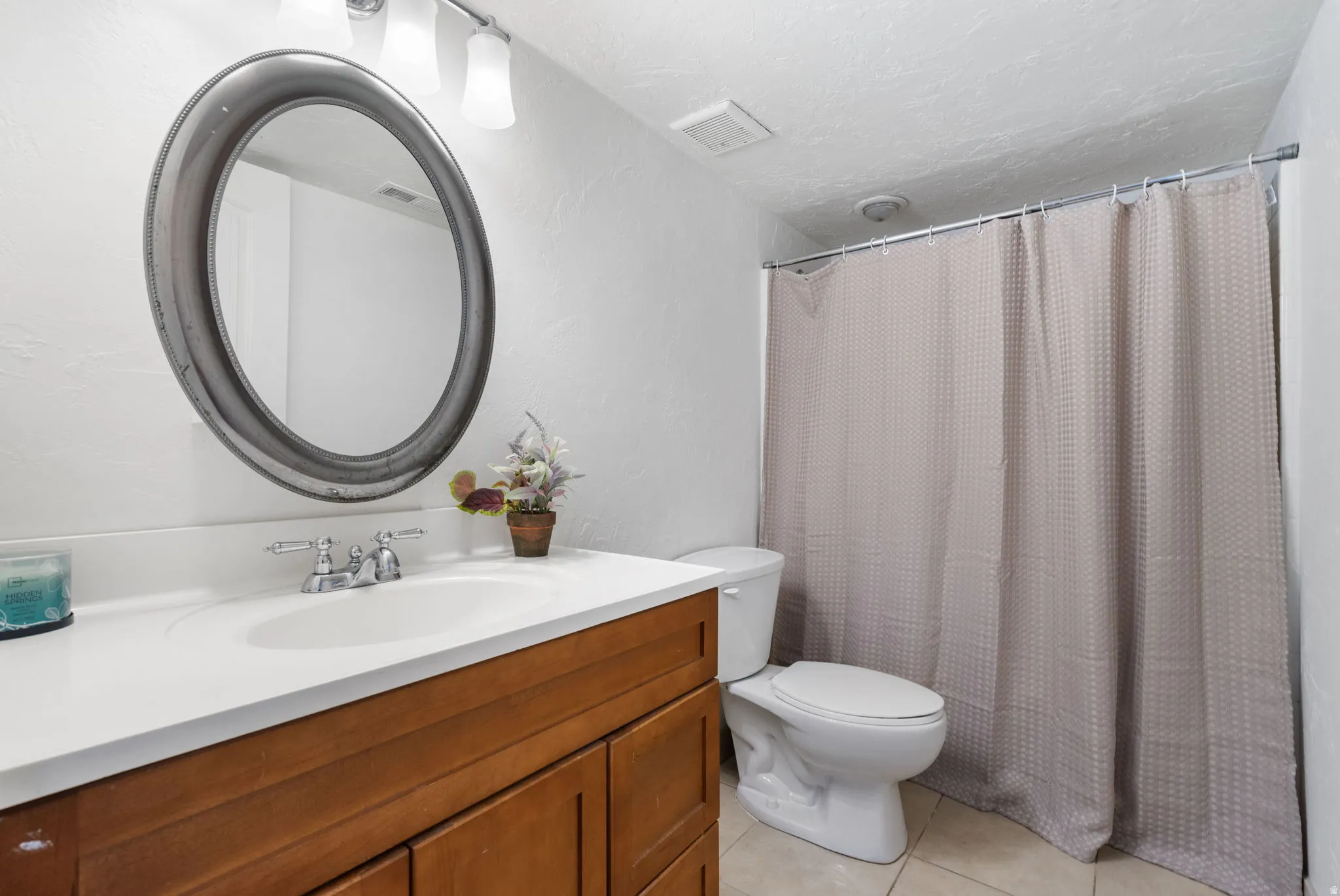 Bathroom with vanity, curtained shower, light tile patterned flooring, and a textured wall