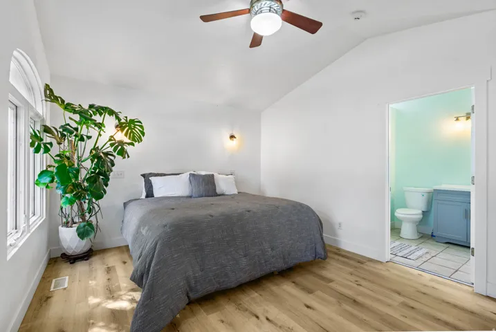 Primary Bedroom featuring light wood-style floors, lofted ceiling, ceiling fan, and connected bathroom