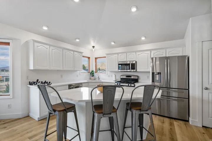 Kitchen with a breakfast bar area, stainless steel appliances, white cabinetry, a center island, and light wood-style flooring