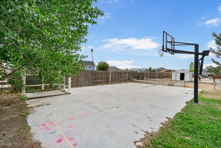 Fenced backyard with a shed, basketball court, and a residential view