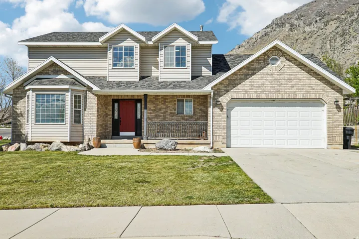 Traditional-style home with covered porch, concrete driveway, a garage, a front lawn, and brick siding