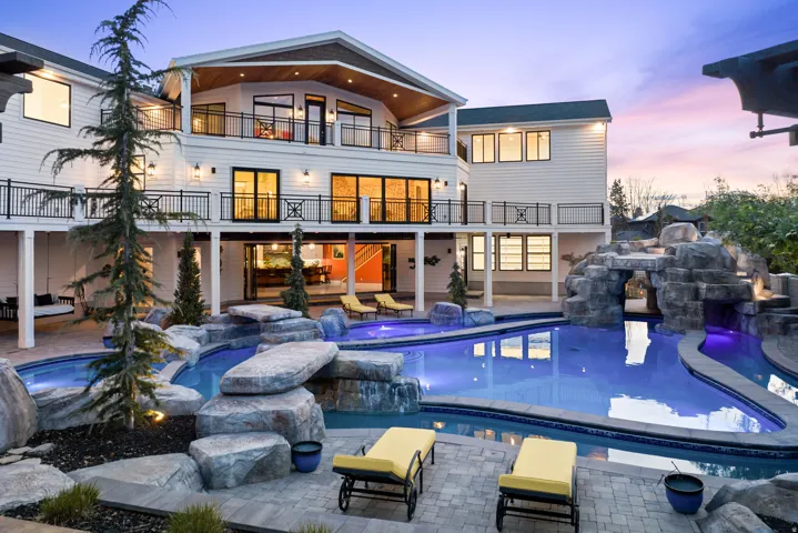 Back of property at dusk featuring a balcony, a patio area, and a pool with connected hot tub