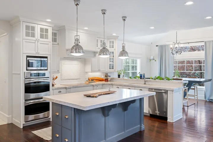 Kitchen with a peninsula, a breakfast bar, glass fronted cabinets, stainless steel appliances, and dual tone cabinets