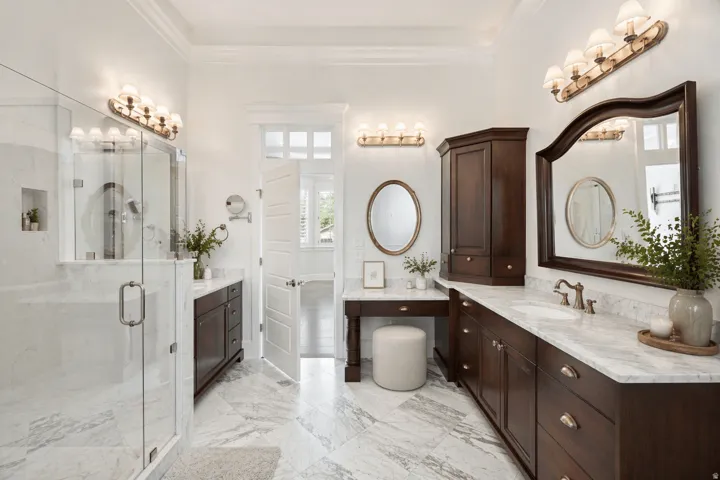 Bathroom with two vanities, a marble finish shower, ornamental molding, and light marble finish floors