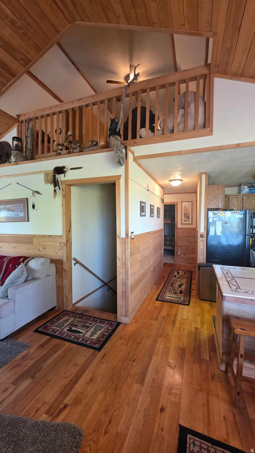 Hallway with a vaulted wooden ceiling, light wood-style floors, wooden walls, and a wainscoted wall