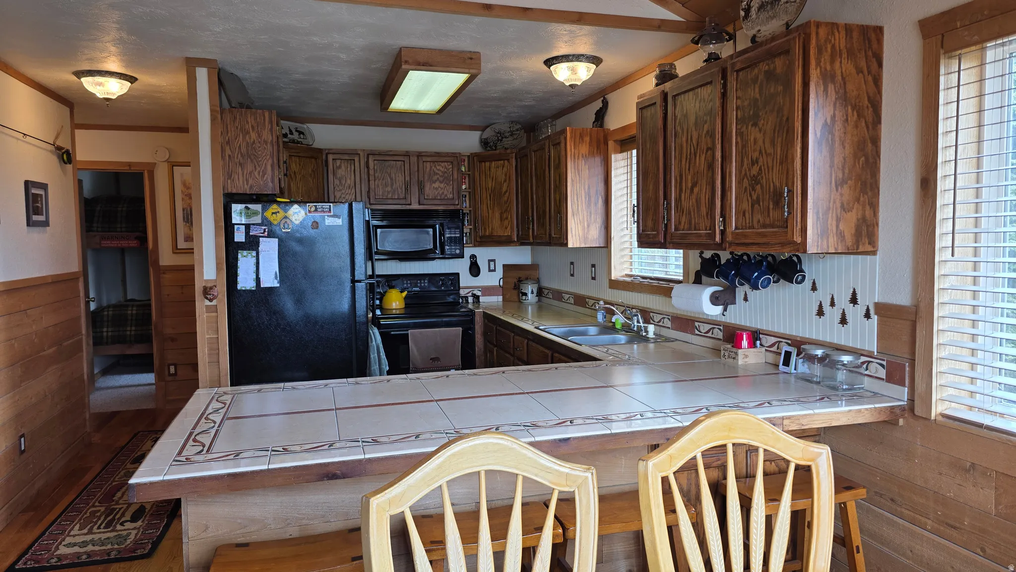 Rustic kitchen featuring wood-finish cabinetry, tile countertops, and a black appliance suite