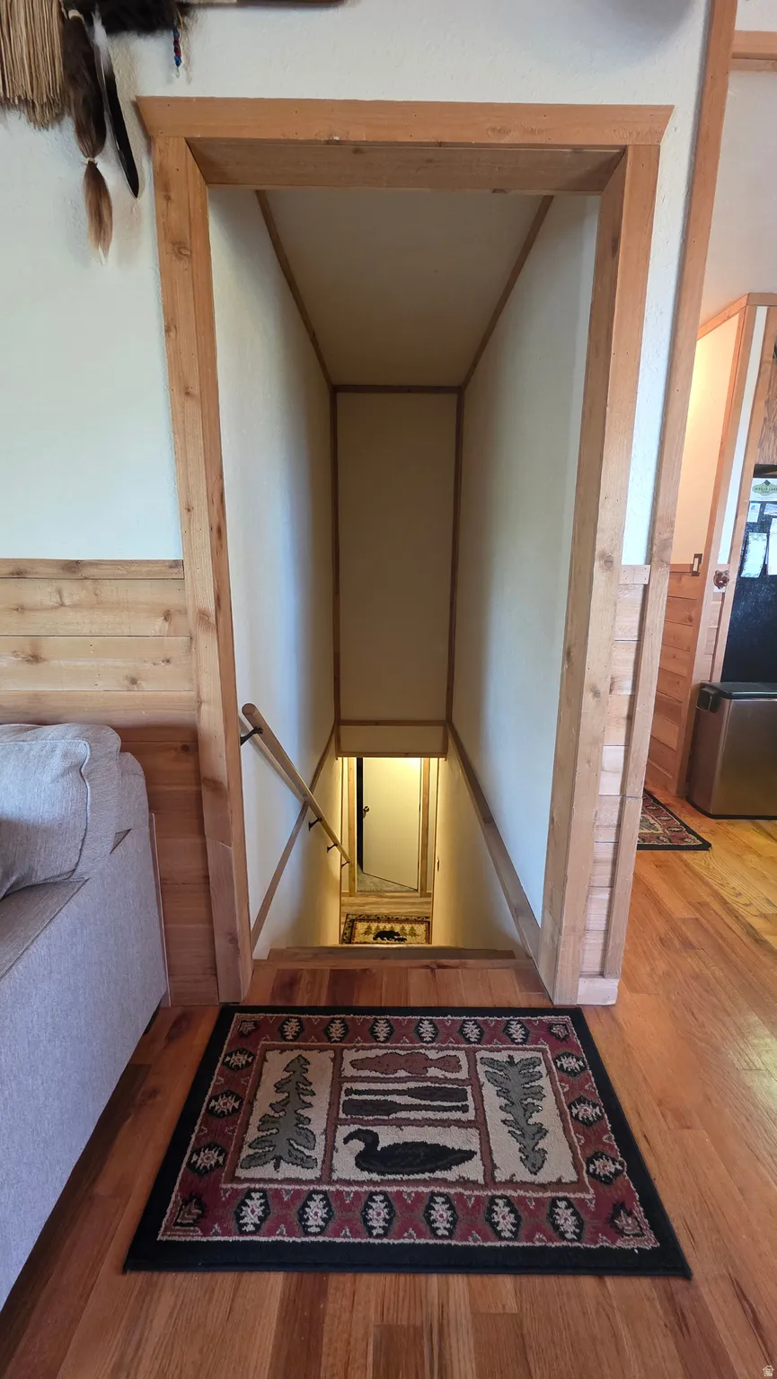 Corridor with wood walls, wood finished floors, an upstairs landing, and a wainscoted wall