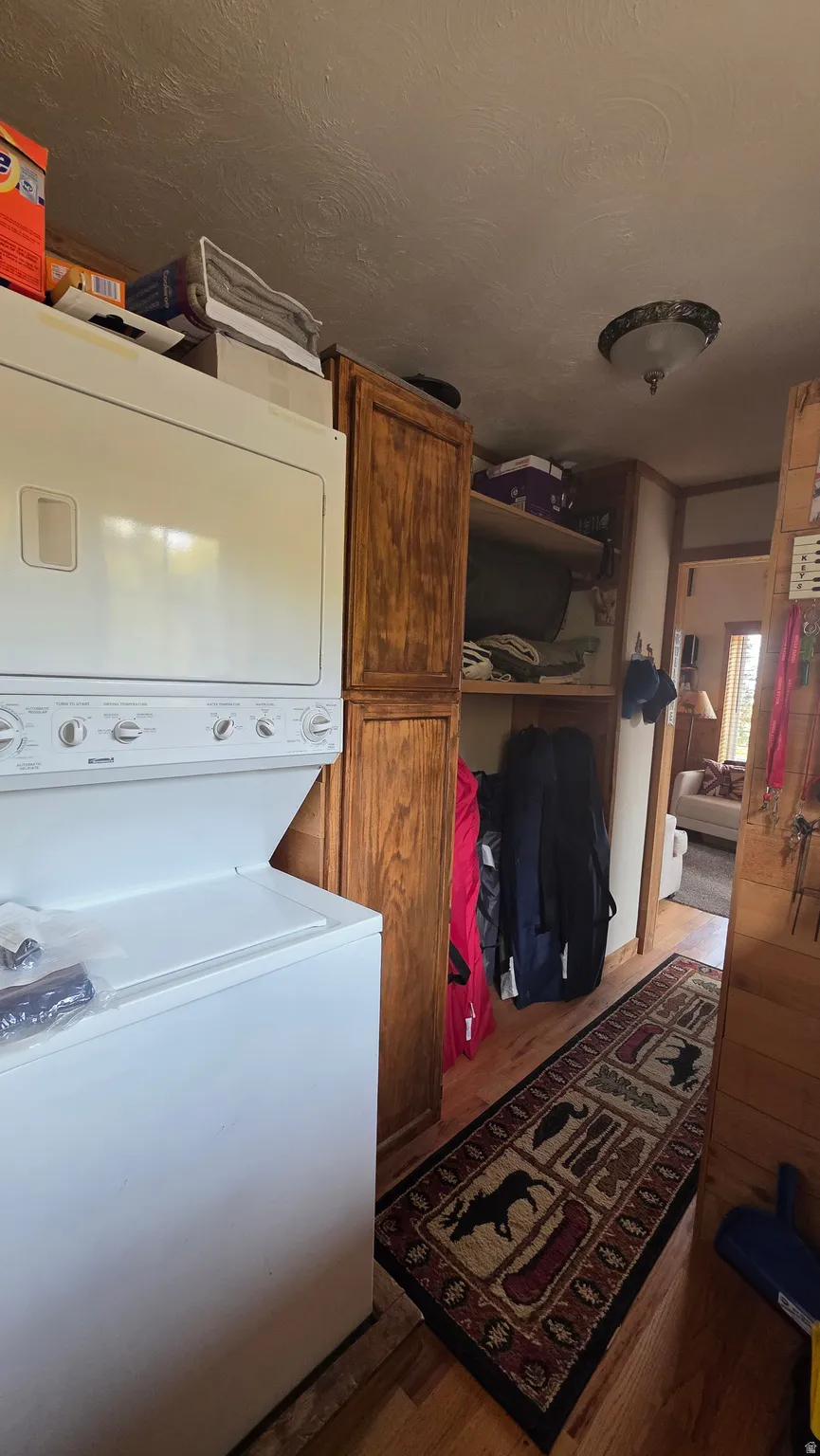 Laundry area with stacked washer and dryer, wood finished floors, and a textured ceiling
