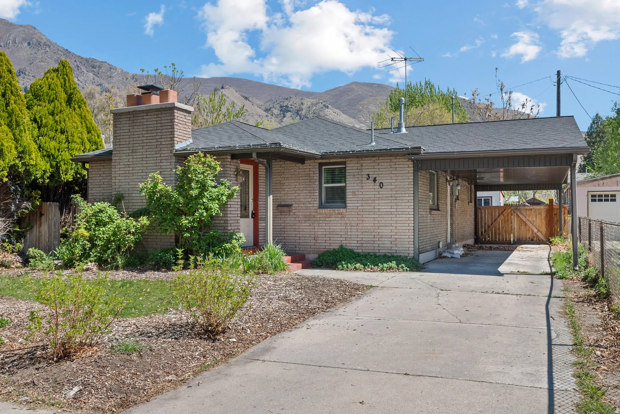 Ranch-style house featuring an attached carport, brick siding, driveway, a gate, and a mountain view