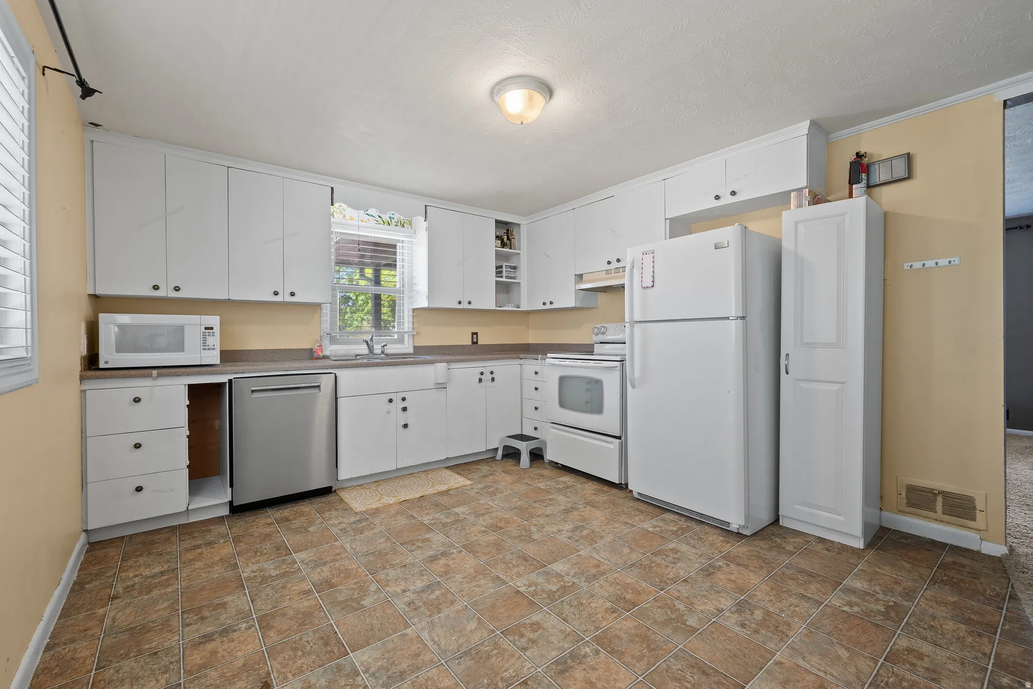 Kitchen featuring white appliances, white cabinets, light countertops, and ornamental molding