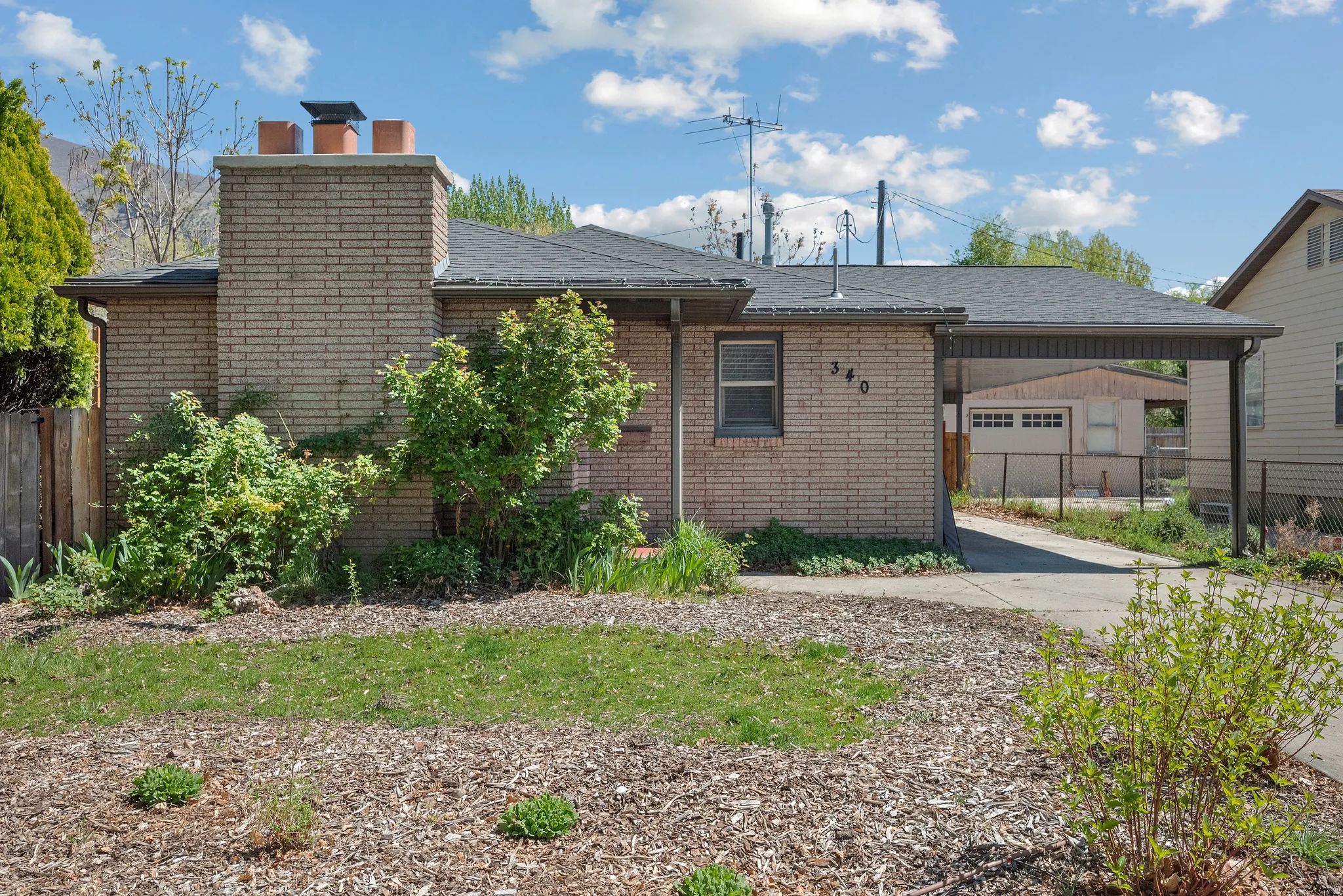 Rear view of property featuring an attached carport, a chimney, brick siding, and roof with shingles