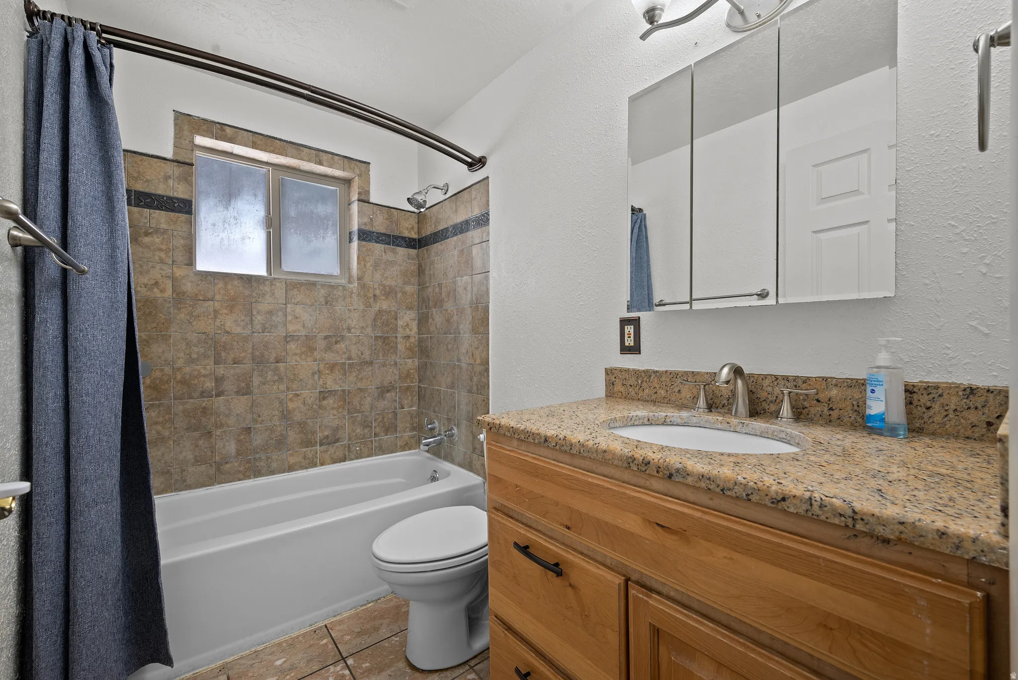 Full bathroom with a textured wall, vanity, and shower / bath combination with curtain