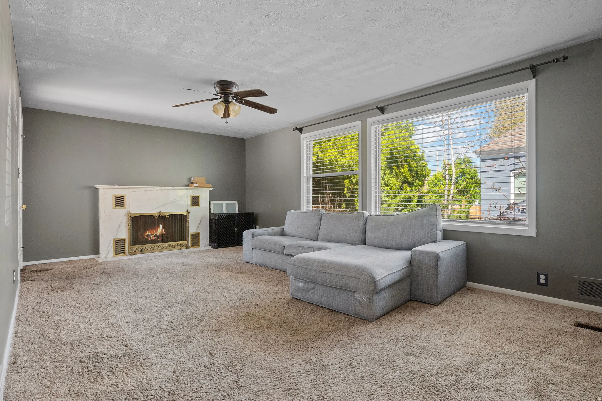 Carpeted living area with a ceiling fan, a high end fireplace, and a textured ceiling