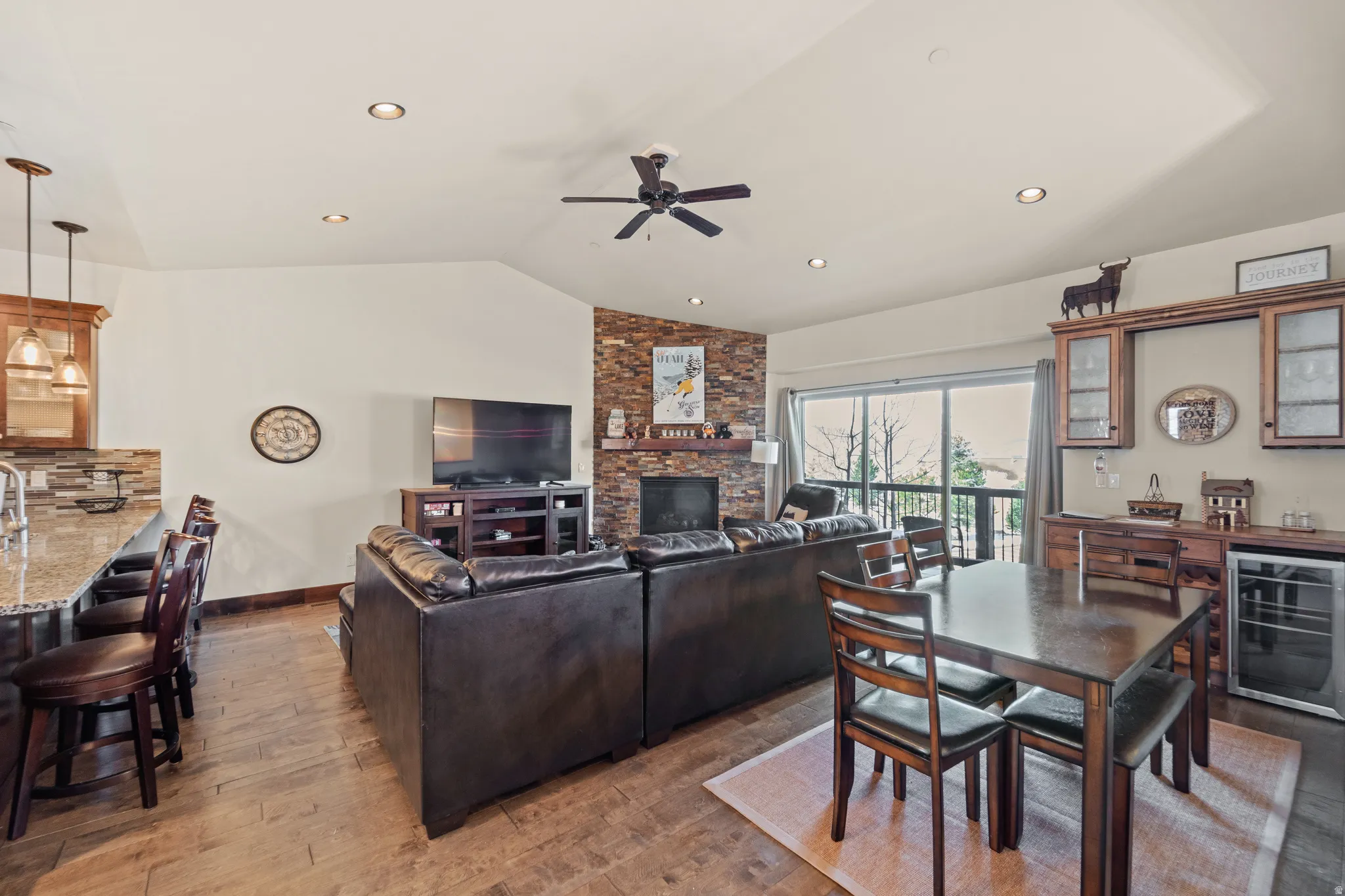 Living room with beverage cooler, vaulted ceiling, dark wood finished floors, a stone fireplace, and ceiling fan