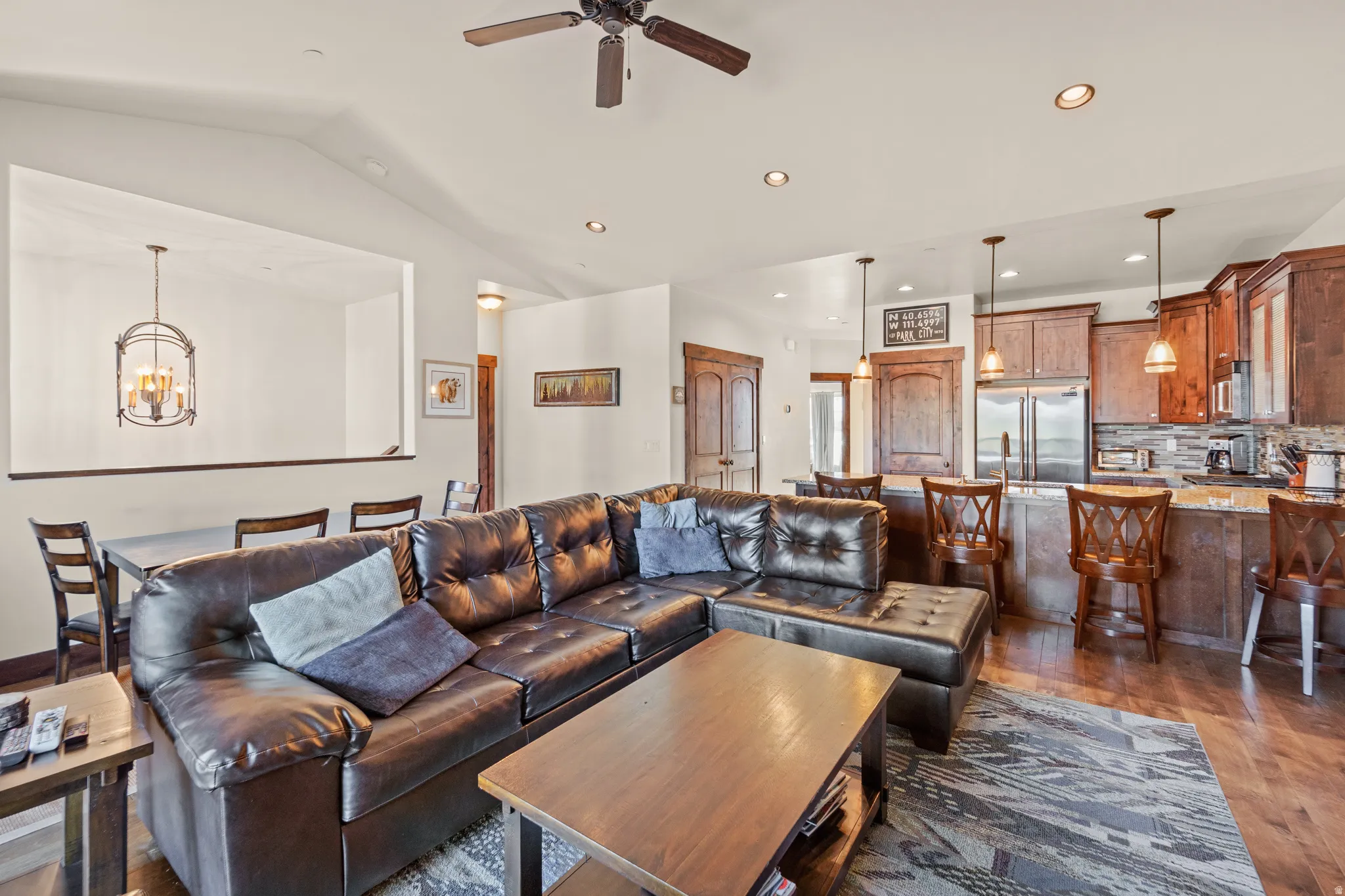 Living room with dark wood-style flooring, ceiling fan, a chandelier, and vaulted ceiling
