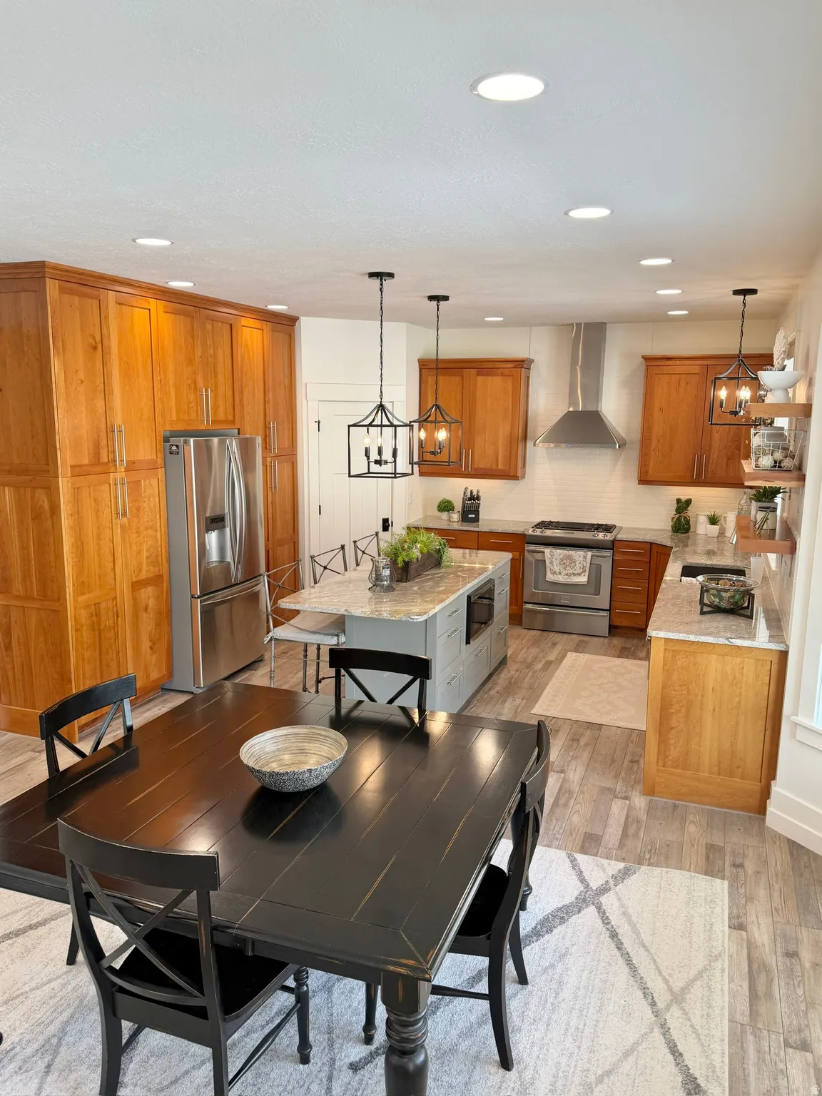 Dual tone kitchen with stainless steel appliances, light stone countertops, dual tone cabinets, light wood-style floors, and a center island
