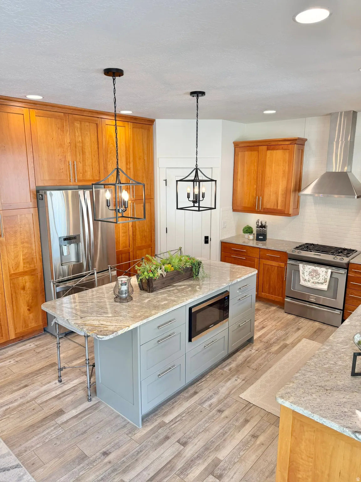 Kitchen with dual tone cabinetry, light stone counters, stainless steel appliances, a center island, and light wood-style floors