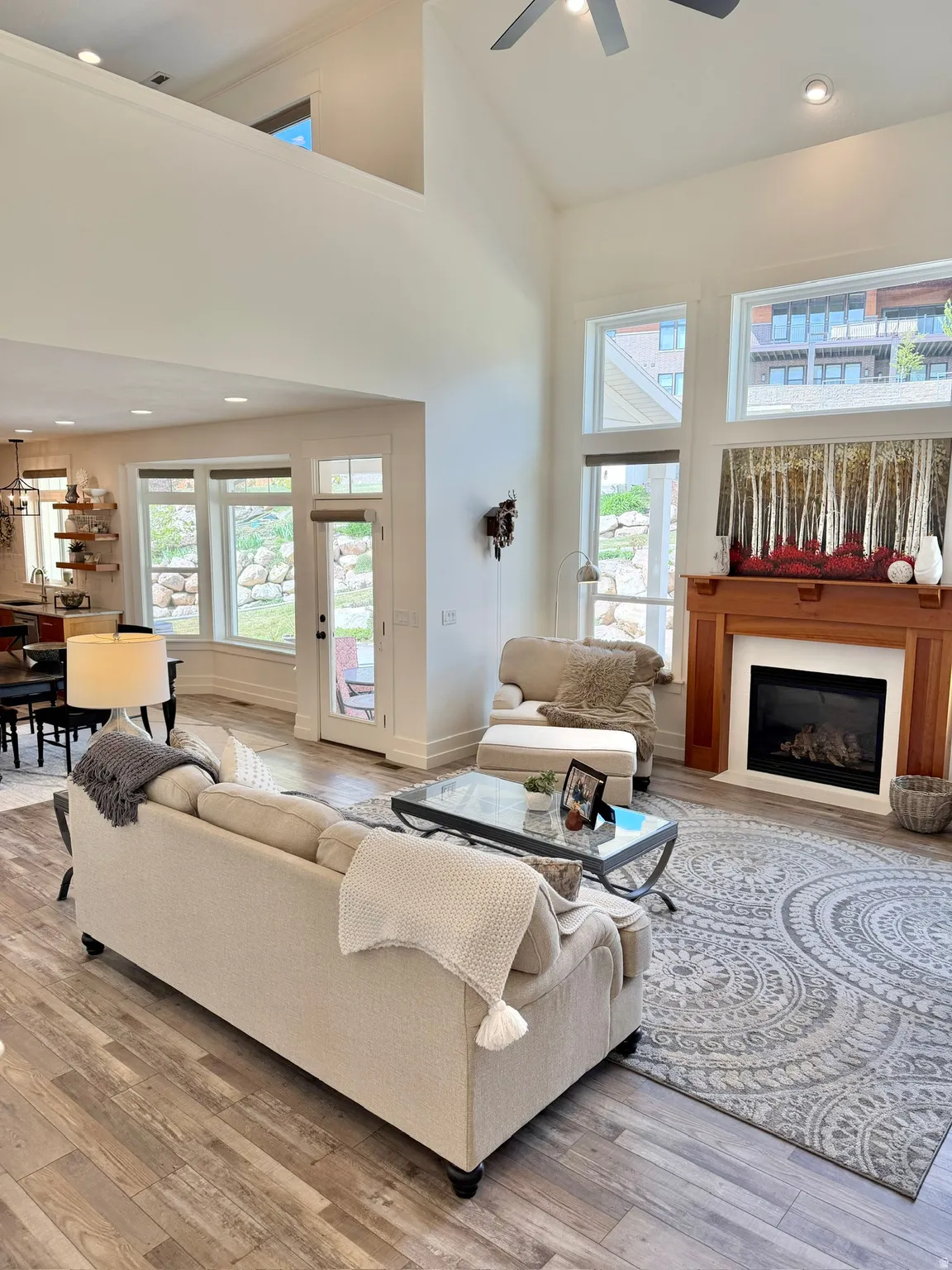 Living area featuring recessed lighting, a high ceiling, light wood-style flooring, a glass covered fireplace, and ceiling fan
