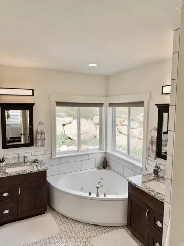 Bathroom featuring two vanities, a whirlpool tub, and tile walls